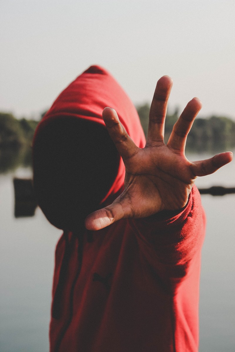 a man wearing a red hoody sweat shirt stretching his hand forward with his palm open, _man in hood stretching hand 4k