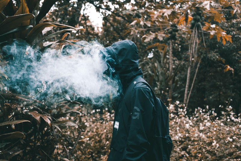a person in a hooded coat outdoors in taipei has their face obscured by white smoke, smoking man 4k