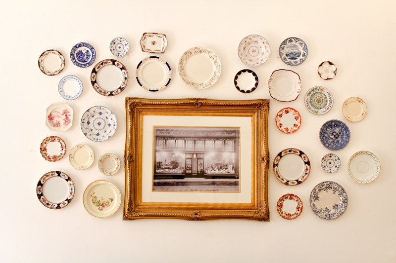 photo in a wooden frame surrounded by colorful decorative plates all hanging on a white wall, london cafe 4k
