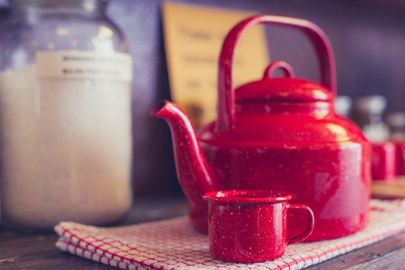 red tea kettle with a red tea cup next to it on a red and white gingham cloth and kitchen wall in the background, cup calling the kettle red 4k