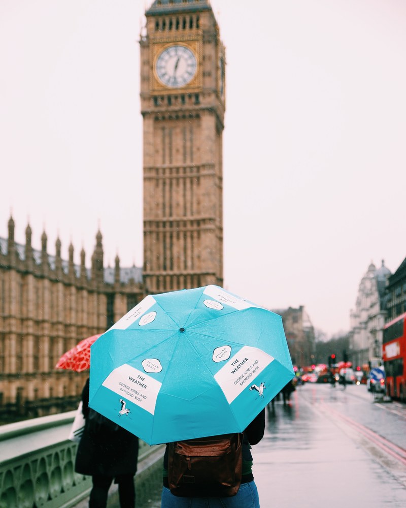 person carries a blue umbrella down a rainy london street, big ben in the rain 4k