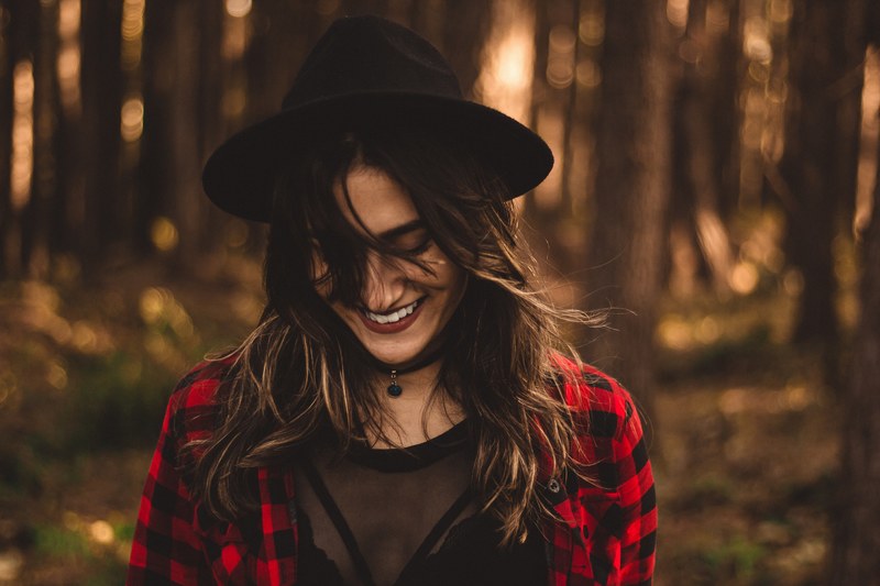 woman in a plaid shirt wearing a hat looks downward while smiling in a sunny forest, smiling in a sunny forest 4k
