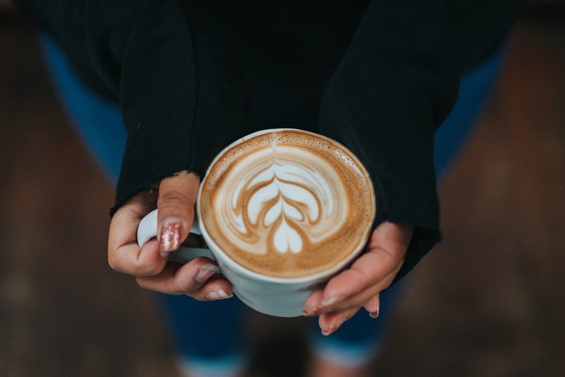 woman wearing long sleeved shirt holding a latte with art drawn in the foam, stacks on stacks on stacks 4k
