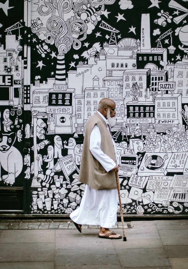 man with cane and white beard walking near black and white street art on brick lane, man with stick on brick lane 4k
