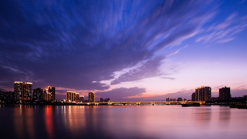 a city at evening reflecting on the waterfront with a purple and pink sky, 4k
