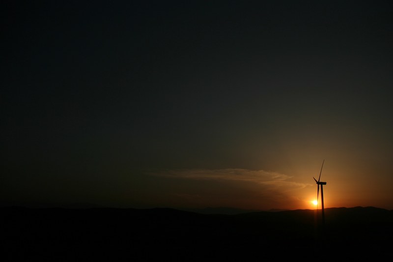 the sunset shines a bright light upon a pikrolimni wind turbine standing in the darkness of the night, light in the dark in pikrolimni 4k