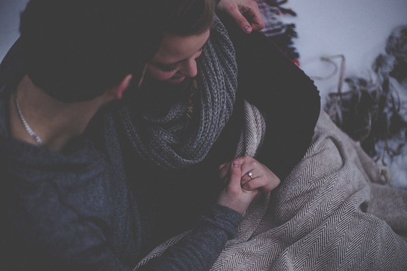 man and woman snuggle under a blanket seated and holding hands she wears an engagement ring, _seated couple snuggling 4k