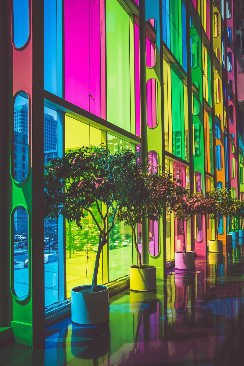 multicolored rainbow glass windows with potted trees in front in urban street, neon tinted windows 4k