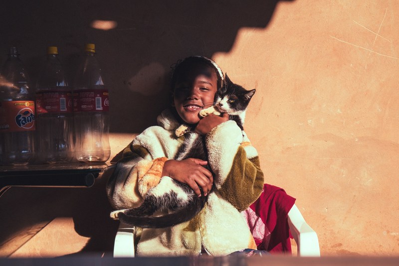 a shadow falls on a seated young girl smiling and cuddling a black and white cat, young girl cuddling a cat 4k