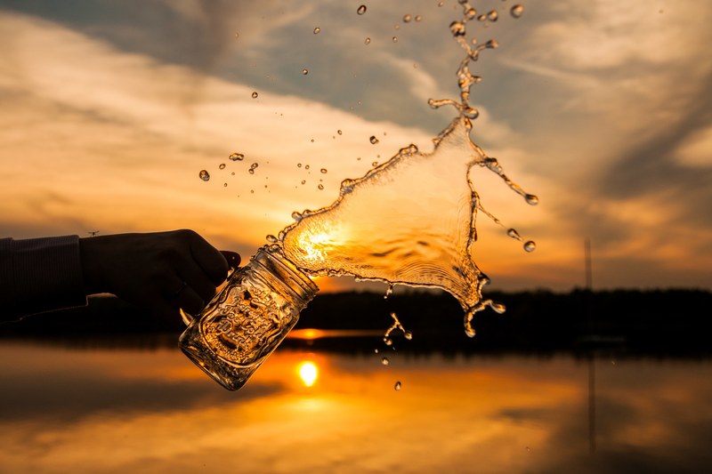 water being splashed out of a mason jar with a sunset backdrop, tossing water at sunset 4k