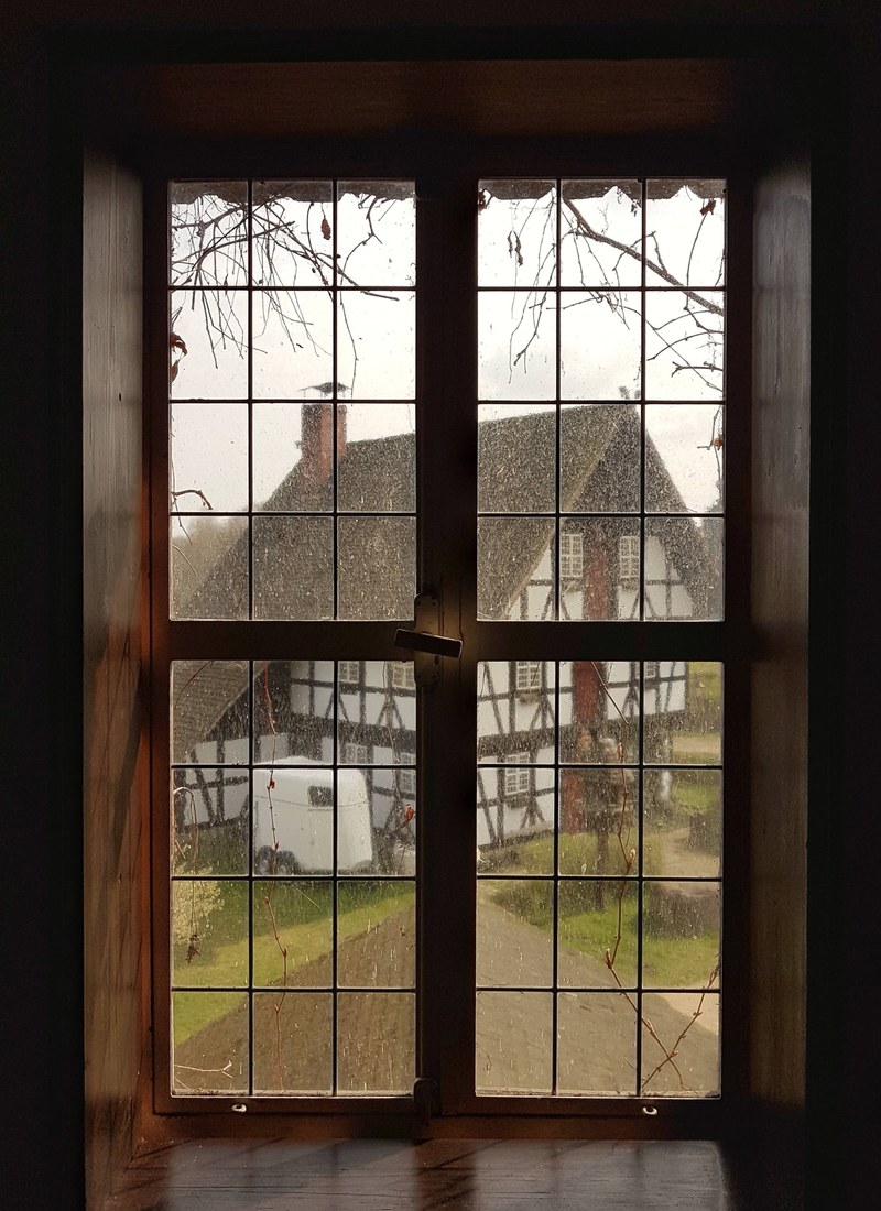 house with a wooden frame and thatched roof seen through a window of a different house, window to the past 4k