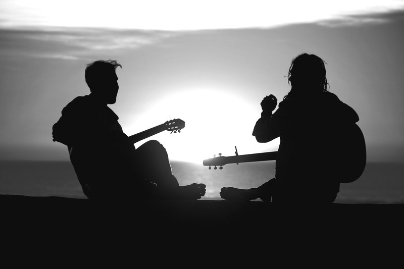 two figures silhouetted against the sun laughing with musical instruments, making music at sunset 4k