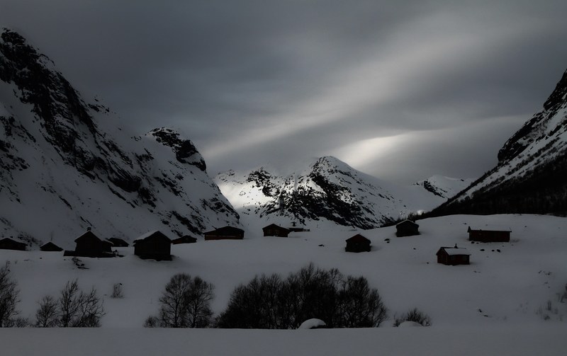 a dim shot of small buildings between snow topped mountains in strynefjellet, gloomy mountain village 4k