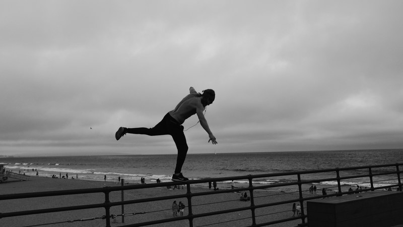 black and white person balancing on barrier at santa monica pier near the ocean, balancing santa monica pier 4k