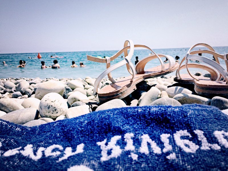 a close up of a blue towel and a pair of sandals on a rocky beach, vacation on a pebble beach 4k