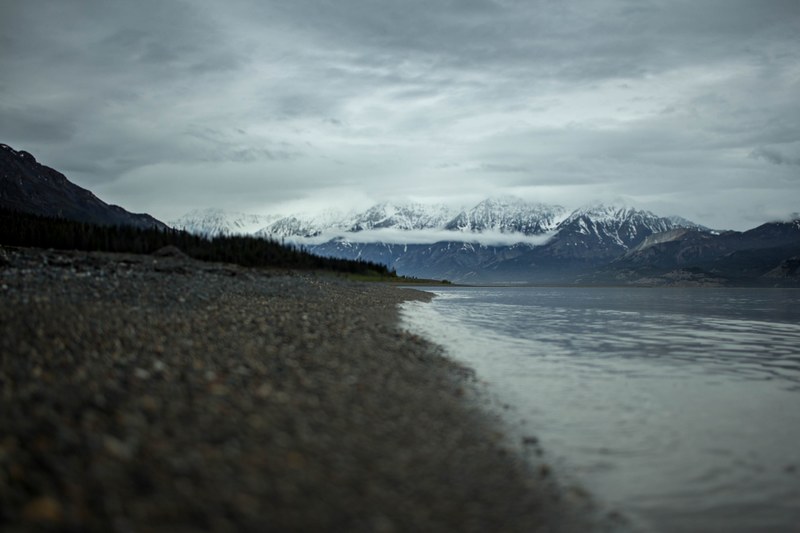 a rocky beach by a lake at yukon with snowy mountains in the distance, misty mountains 4k