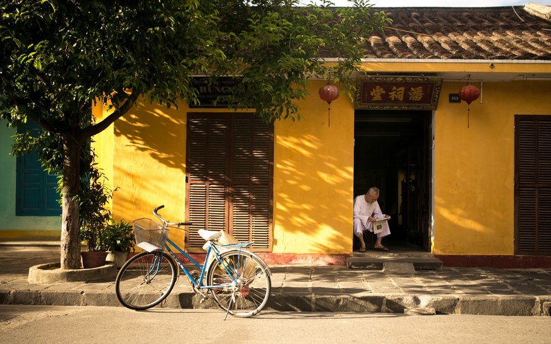 a man sitting on his stoop reading the newspaper and a bicycle leaning on a tree in asia, man reading paper 4k