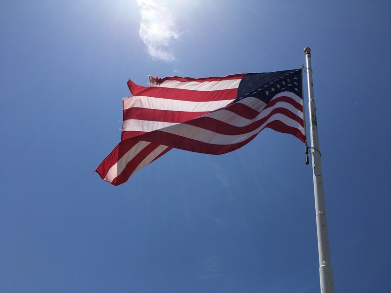 american flag flying in the wind against a sunny blue sky, worn flag 4k