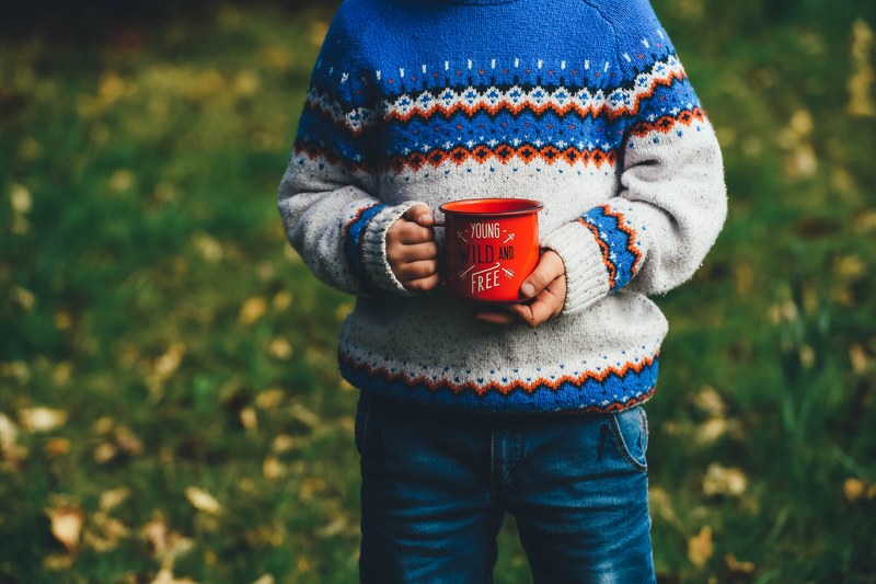 a child holding a red enamel cup with young wild and free written on it, child with a red cup 4k