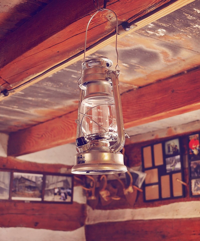an old rustic lantern hangs in a wooden lodge with photos on the walls, camping in style 4k
