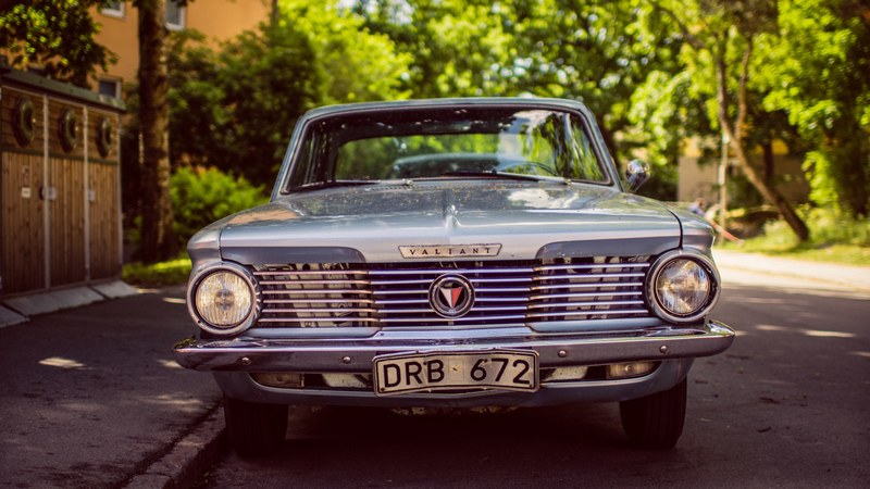 vintage blue valiant with shiny silver grille parked on the sidewalk in front of trees, vintage blue valiant 4k