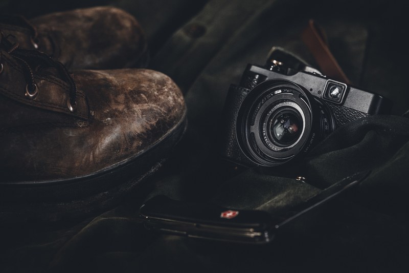 a vintage camera beside leather boots and a pocket knife on a jacket, the edc 4k
