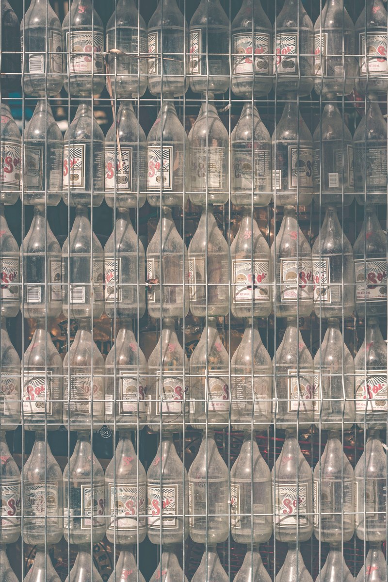 a dusty wall of empty sol beer bottles stuck between an old chain link fence, _tulum mexico 4k