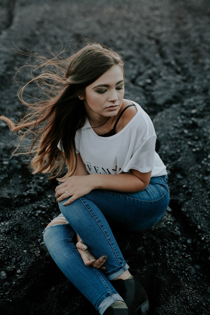 young woman holding her knees while sitting on a black sand beach, alone at the beach 4k