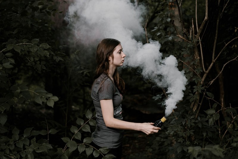 a woman among greenery holds a smoke grenade letting off white smoke, woman with smoke grenade 4k
