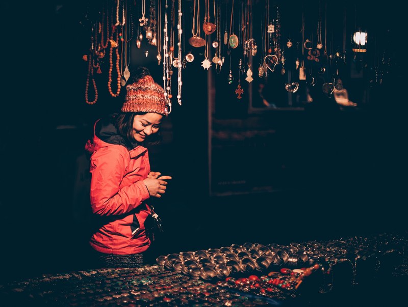 a woman in a knit hat smiles while browsing accessories at a stall in camden town, charms of joy 4k