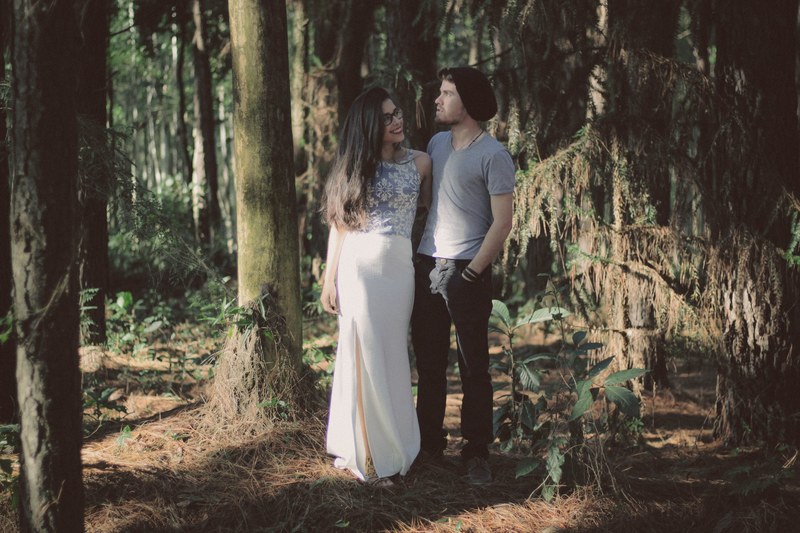 a young woman in a dress puts her arm around a young man in a hat in a wooded area, stylish couple in the woods 4k