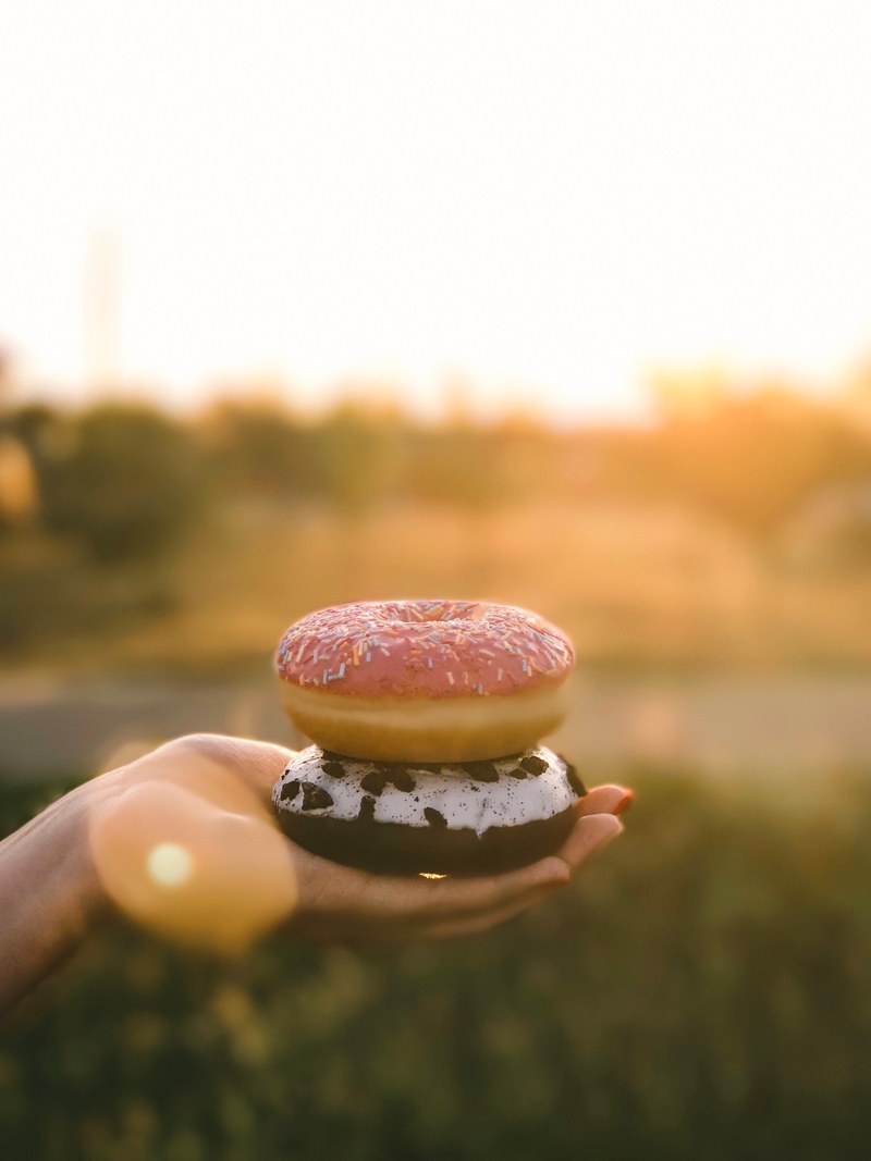 a person holding two donuts outside, _holding donuts in hand 4k