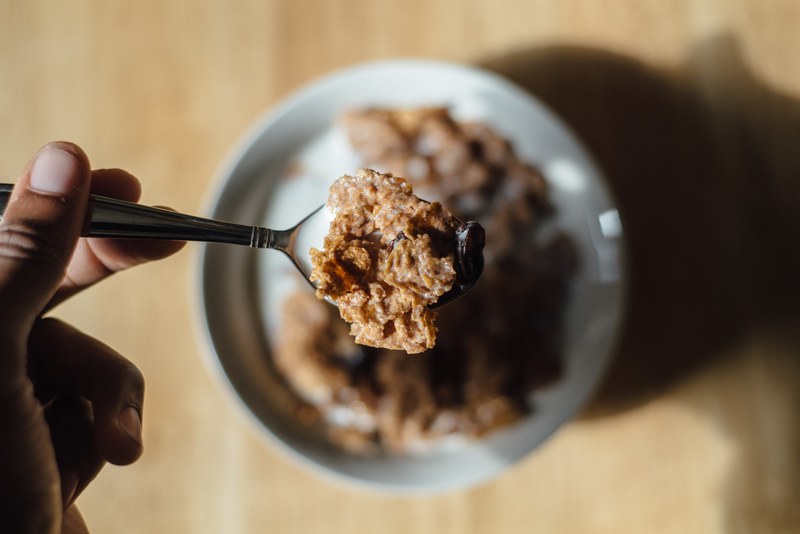 a person holding a spoon full of cereal over a bowl of cereal and milk, cereal with milk 4k