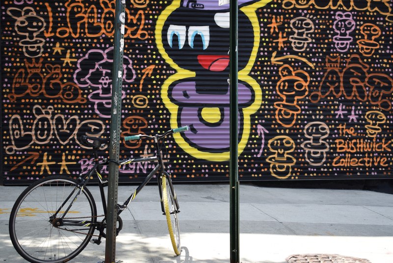 cartoonish colorful purple graffiti covering urban wall with bike leaning against post on sidewalk, cartoon graffiti with bike 4k