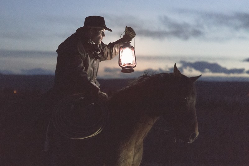 a man in a cowboy hat holds a lasso in one hand and a lamp in another while riding a horse, illuminating the way 4k