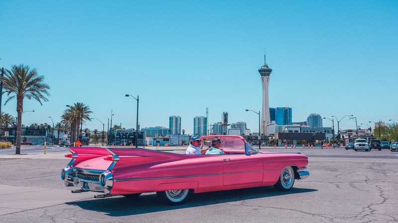 pink vintage cadillac car on pavement on clear day in arts district with tower on skyline, vintage pink car 4k