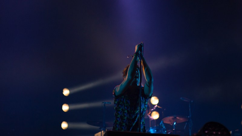 a vocalist singing into a microphone on a stand pointed downwards, frontman in blue light 4k