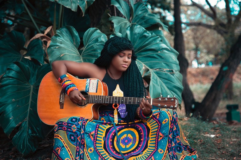 a woman with long twists in her hair and an ornate skirt plays a guitar outdoors, woman playing guitar 4k