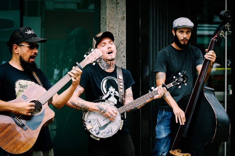 three young men with a guitar a banjo and a double bass busking on street, acoustic street band performing 4k