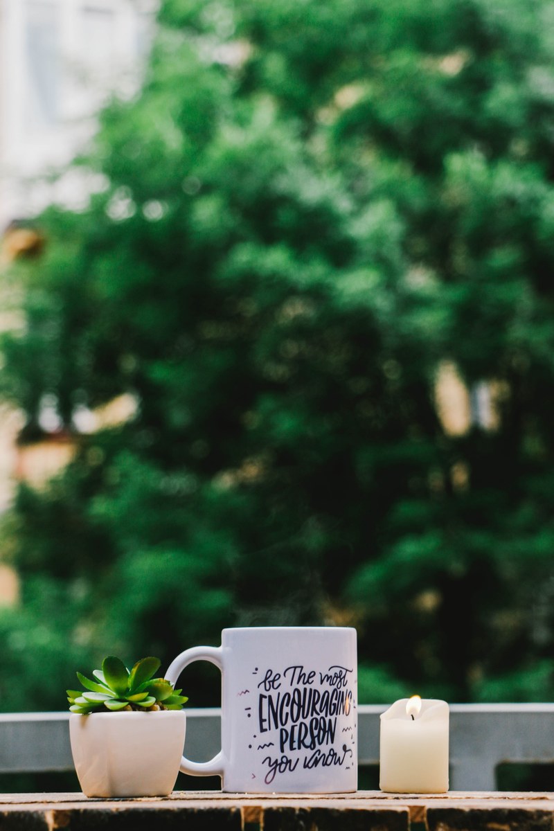a white mug with be the most encouraging person you know written on it next to a potted plant and a candle, be the most encouraging person you know 4k