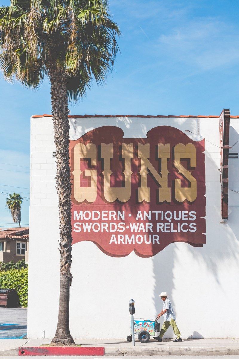 a man pushing an ice cream cart near a building with a large advertisement, guns amp icecream 4k