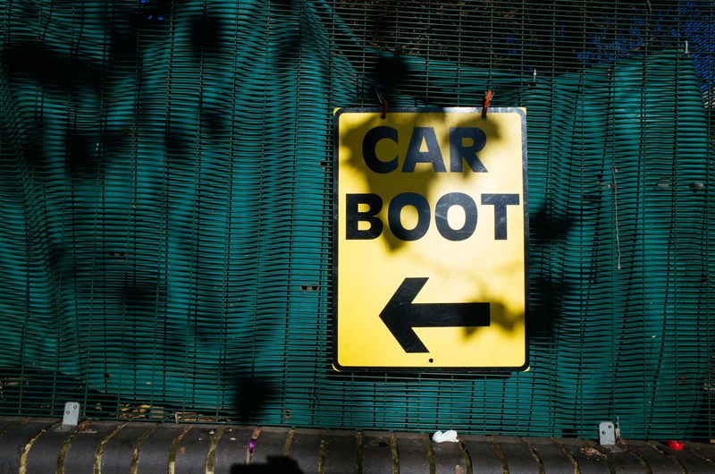 black mesh fencing with green tarp behind and a yellow car boot sign with an arrow, car boot sale 4k