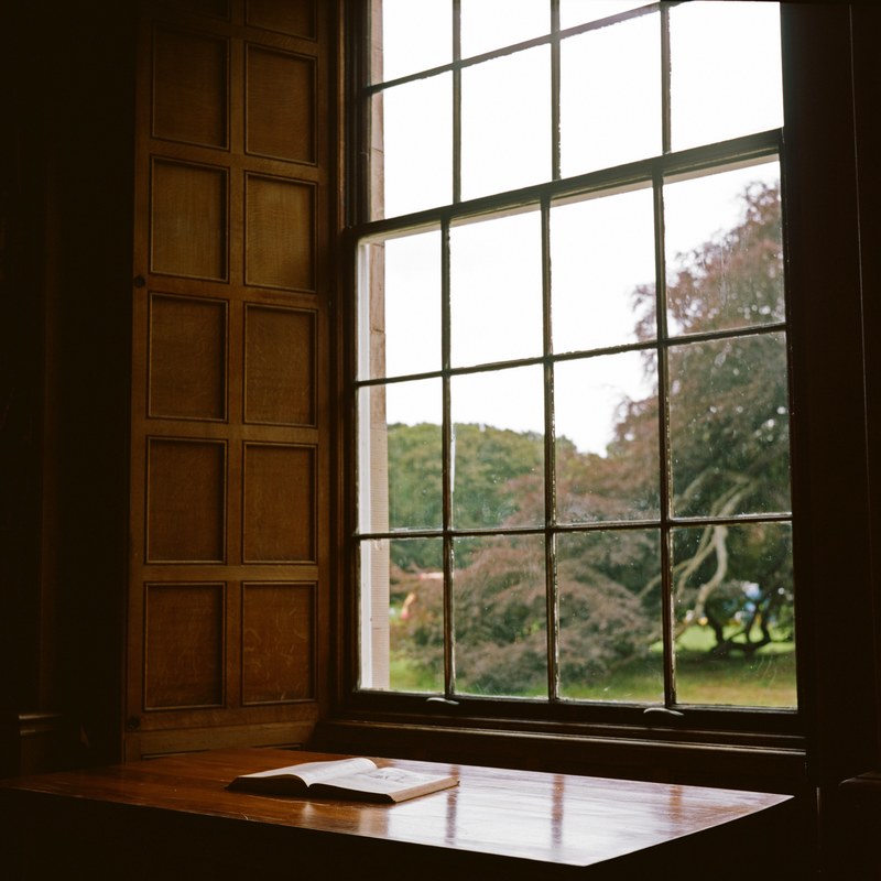 an open book on a glossy wooden surface near a window, book by a window 4k