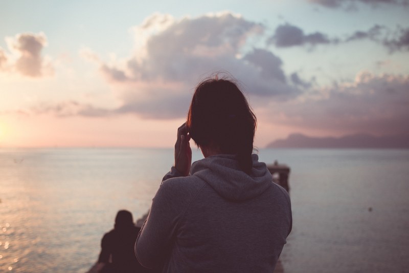 woman in a grey hoodie looking at the ocean sunset, at sea during sunset 4k