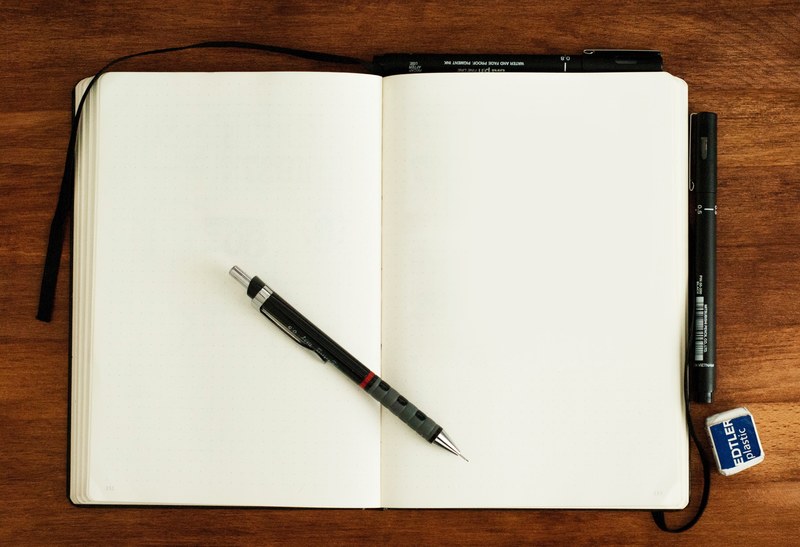 a journal open to a blank page on a table with three pens and an eraser, the open sketch book 4k