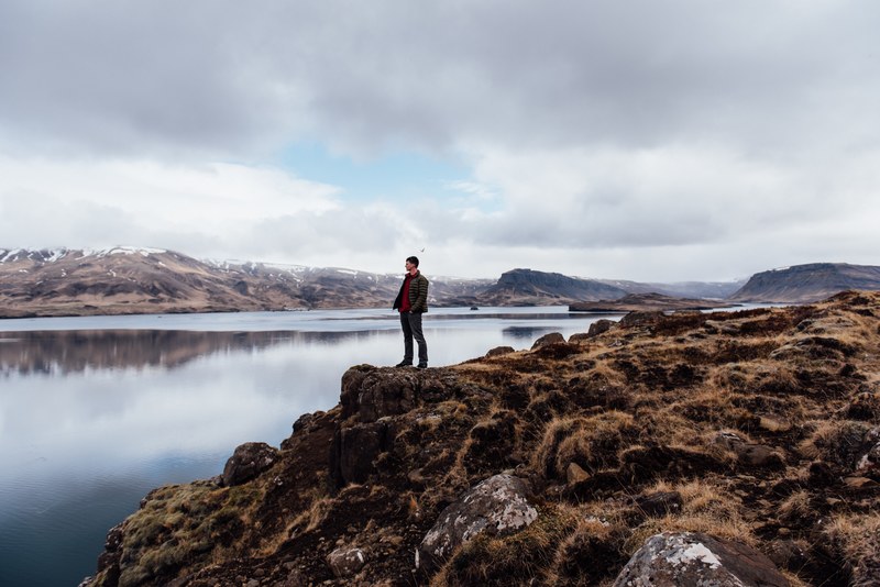 person stands on the rocky seaside near the water, reflections by the water 4k