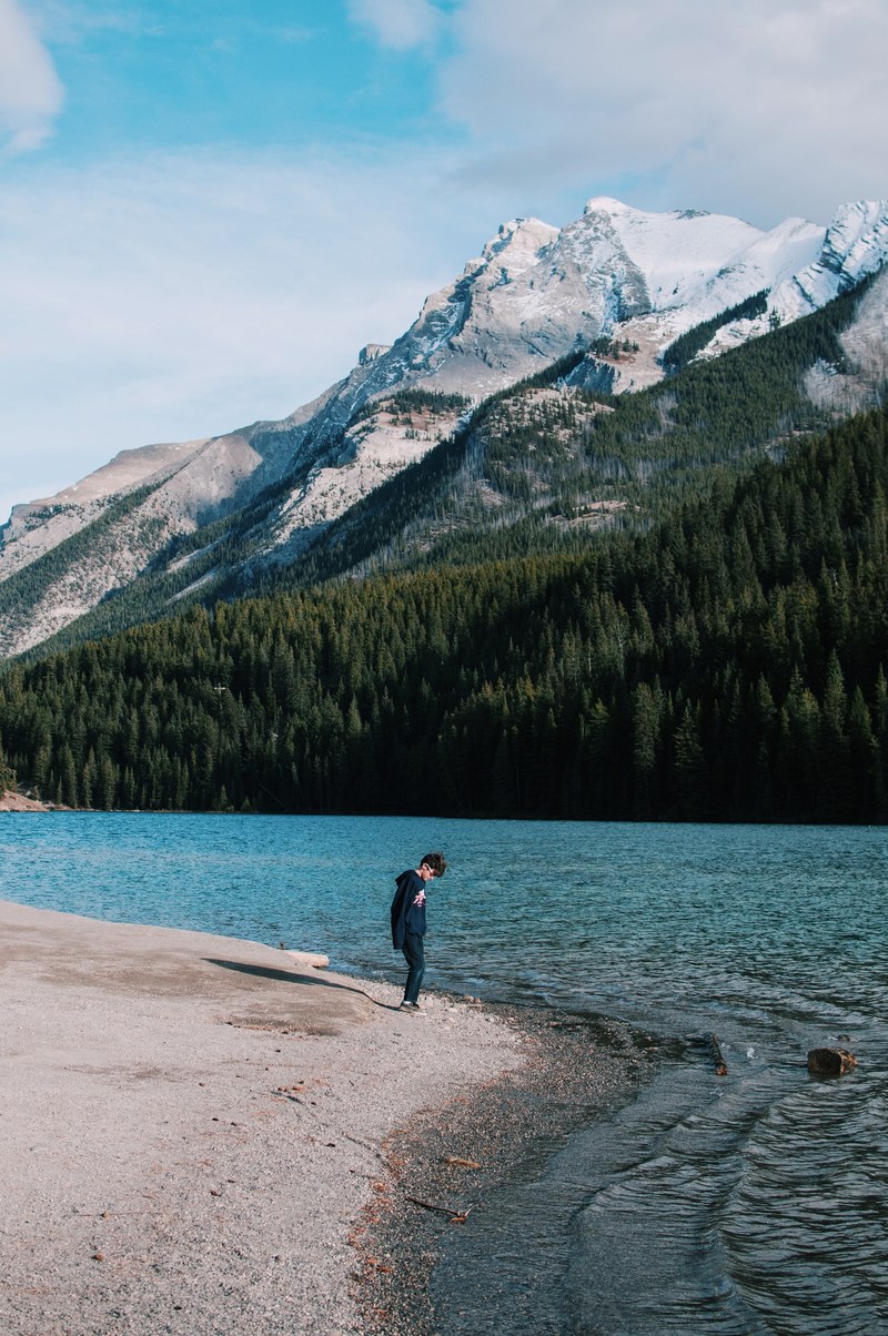 a young man standing on the shore of a mountain lake and looking down, curiosity amp enormity 4k