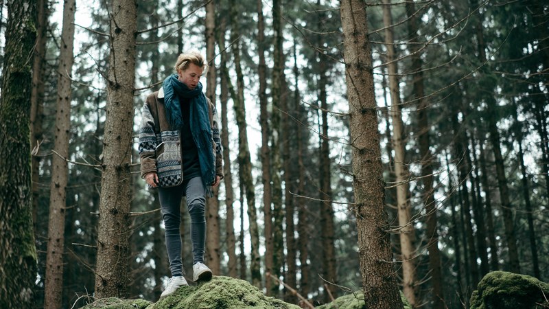 a young man standing on a mossy rock in a coniferous forest, bohemian man on a mossy rock 4k