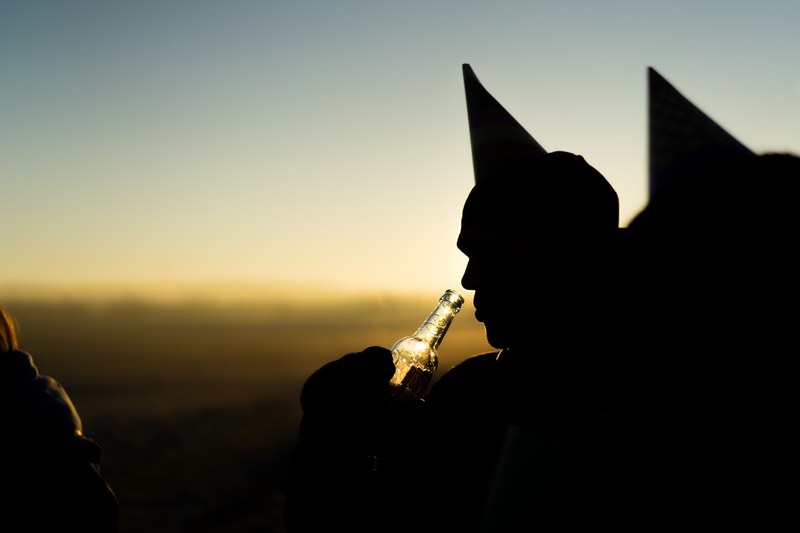 a silhouette of a man drinking from a beer bottle wearing a party hat, cheers 4k
