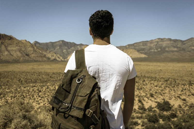 a man with a backpack on his shoulder looking at the semi arid landscape in front of him, exploring the canyon 4k